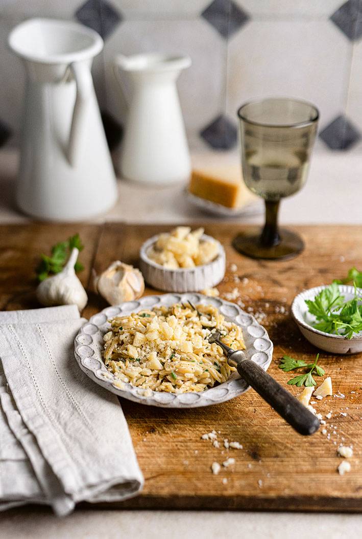 Ein Teller Pasta auf einem rustikalen Holztisch, mit Knoblauchknollen, einem Weinglas und Petersilie im Hintergrund